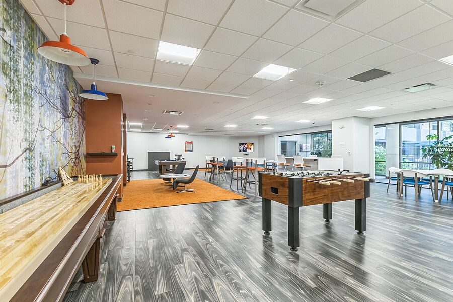 Modern game room with foosball table, shuffleboard, hardwood floors, and large windows in a recreational facility.