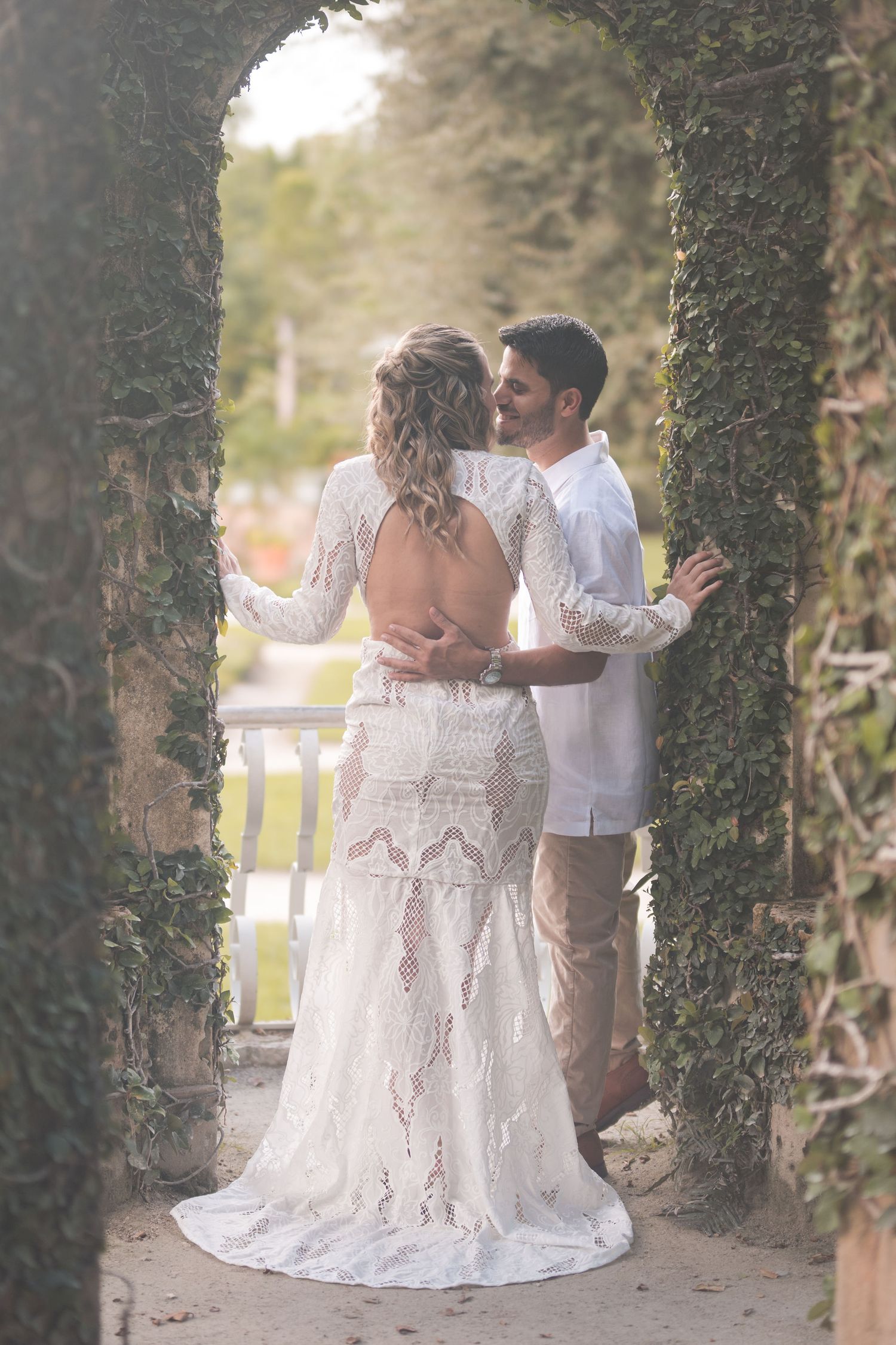 Bride and groom stand beneath an ivy covered archway at Vizcaya Gardens, sharing a quiet moment surrounded by lush greenery.