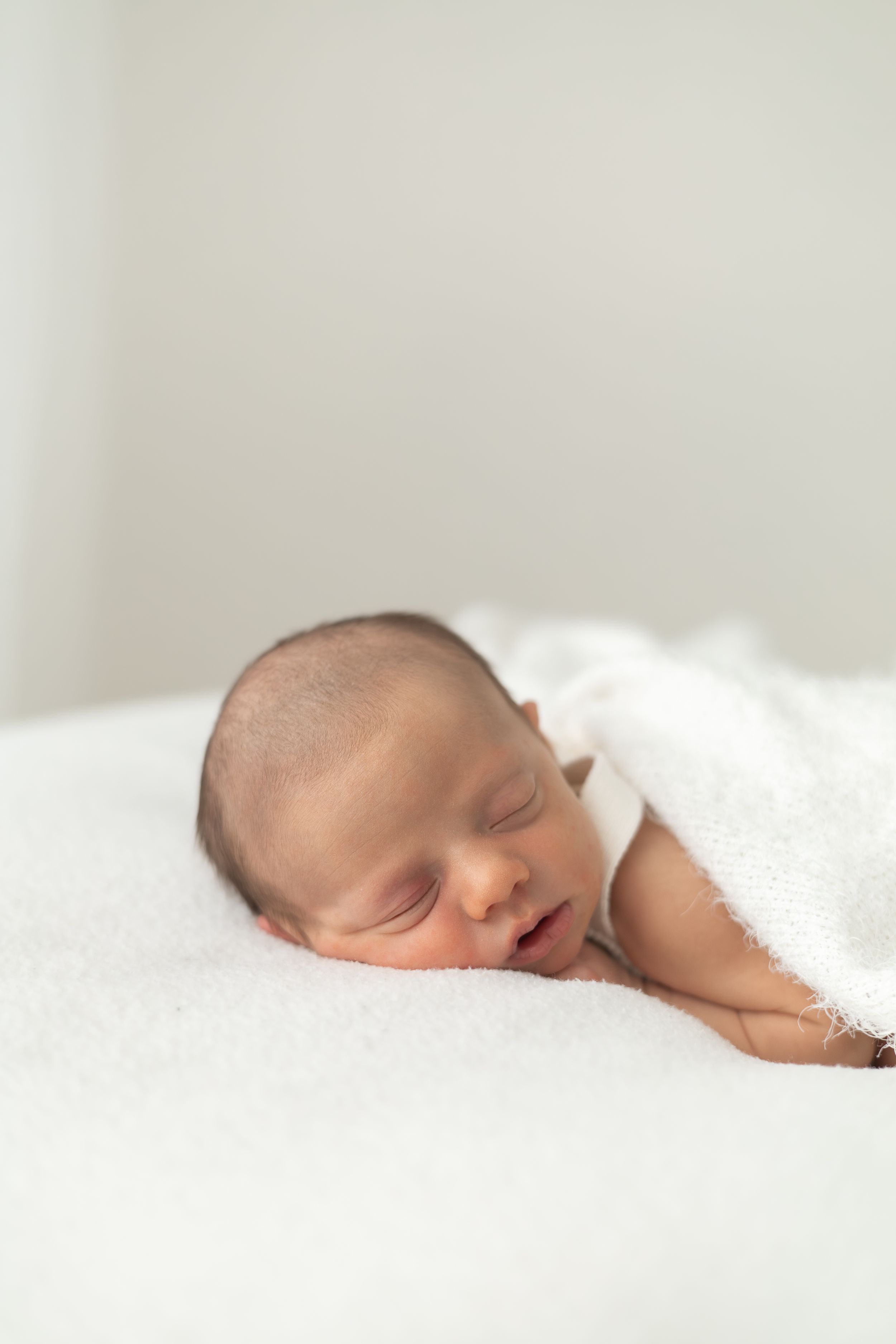 Peaceful newborn baby sleeping wrapped in a soft white blanket on a white surface natural newborn photography Nottingham