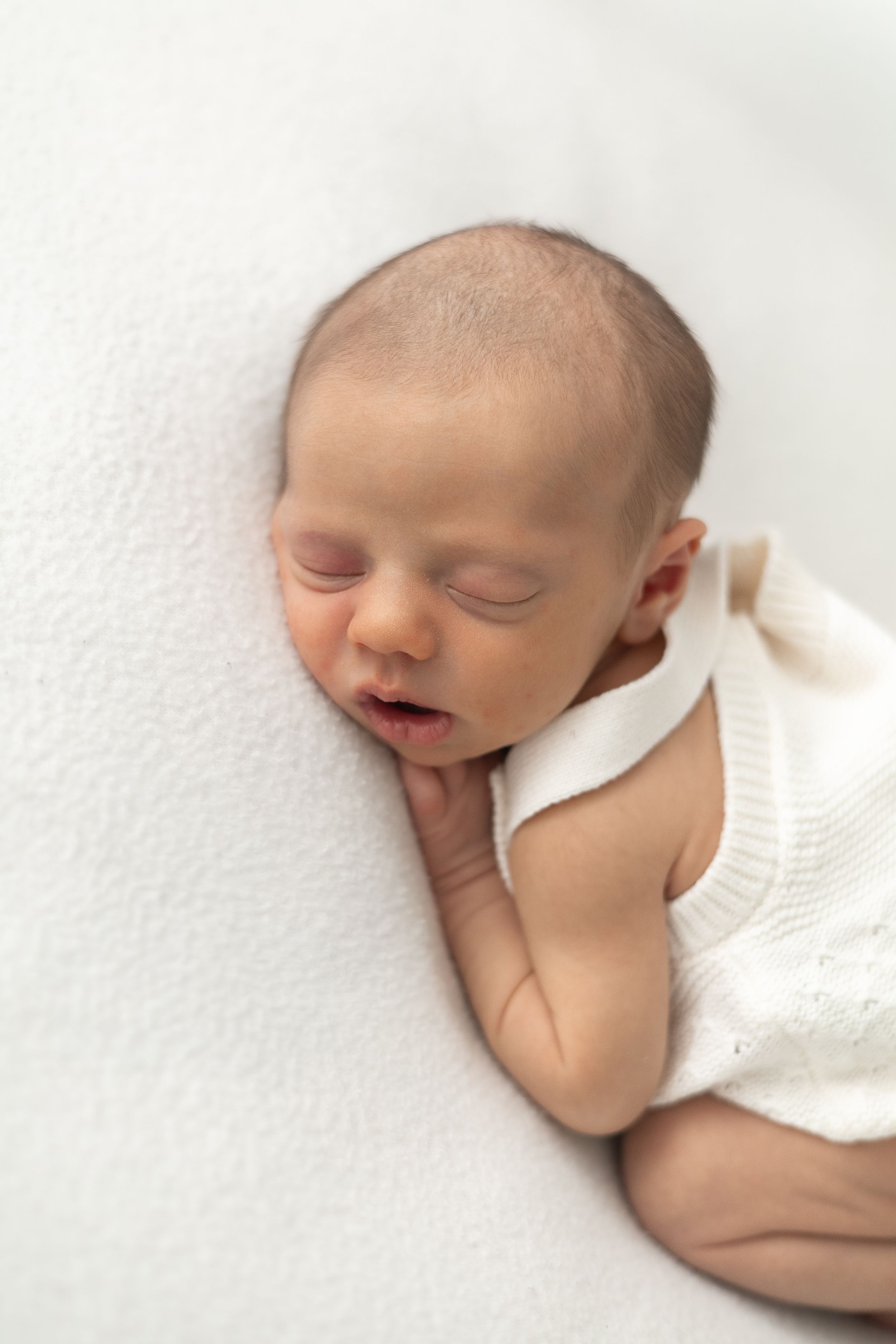 Sleeping newborn baby in white knit romper lying on soft white blanket during natural newborn photography Nottingham