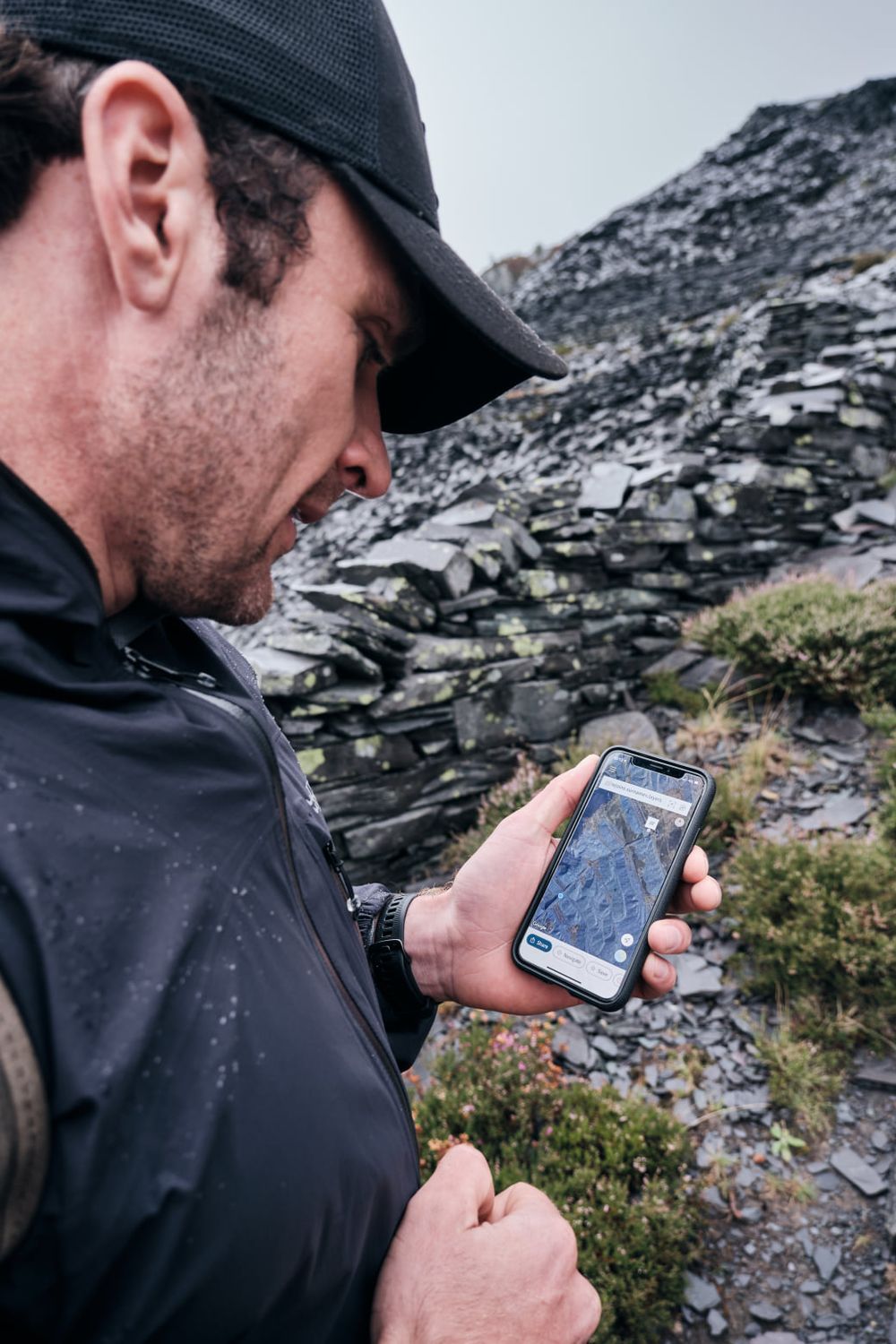Hiker in black jacket checks navigation map app on smartphone while exploring rocky mountain terrain.