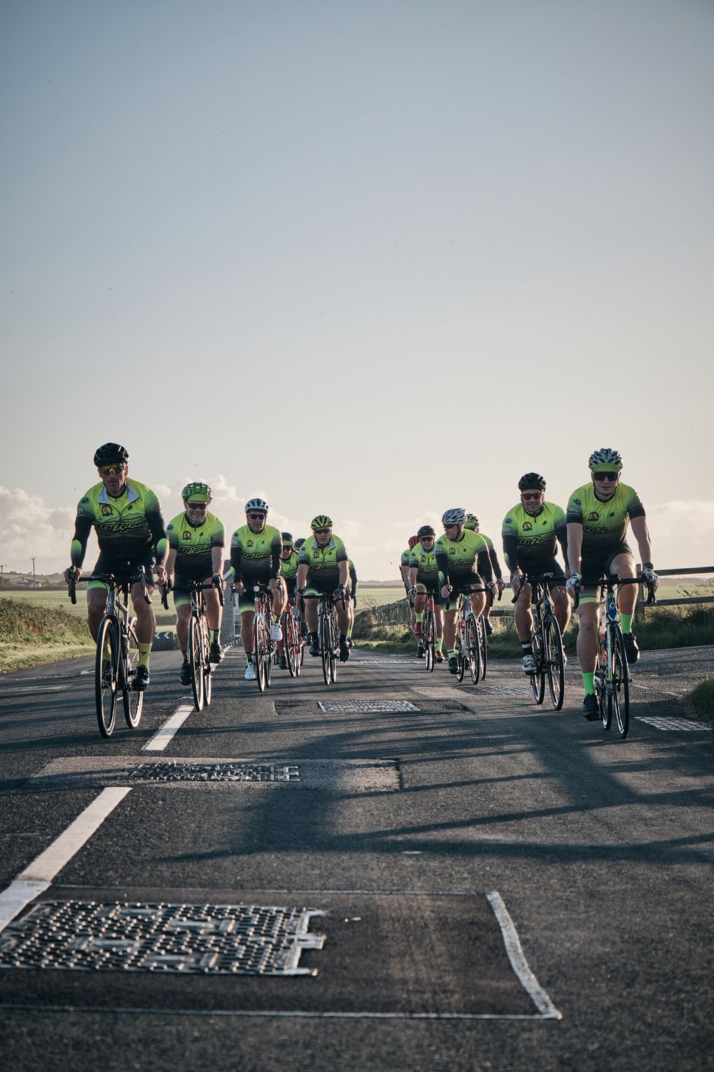 Group of cyclists in green kit riding together on a rural road under a clear sky.