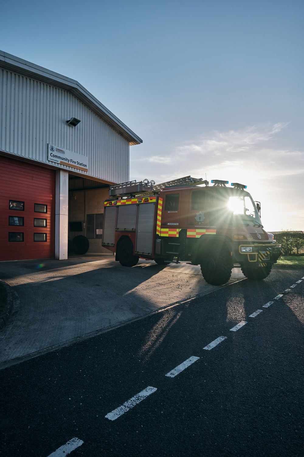 Fire truck parked outside a fire station at sunset with sun flare illuminating the vehicle.