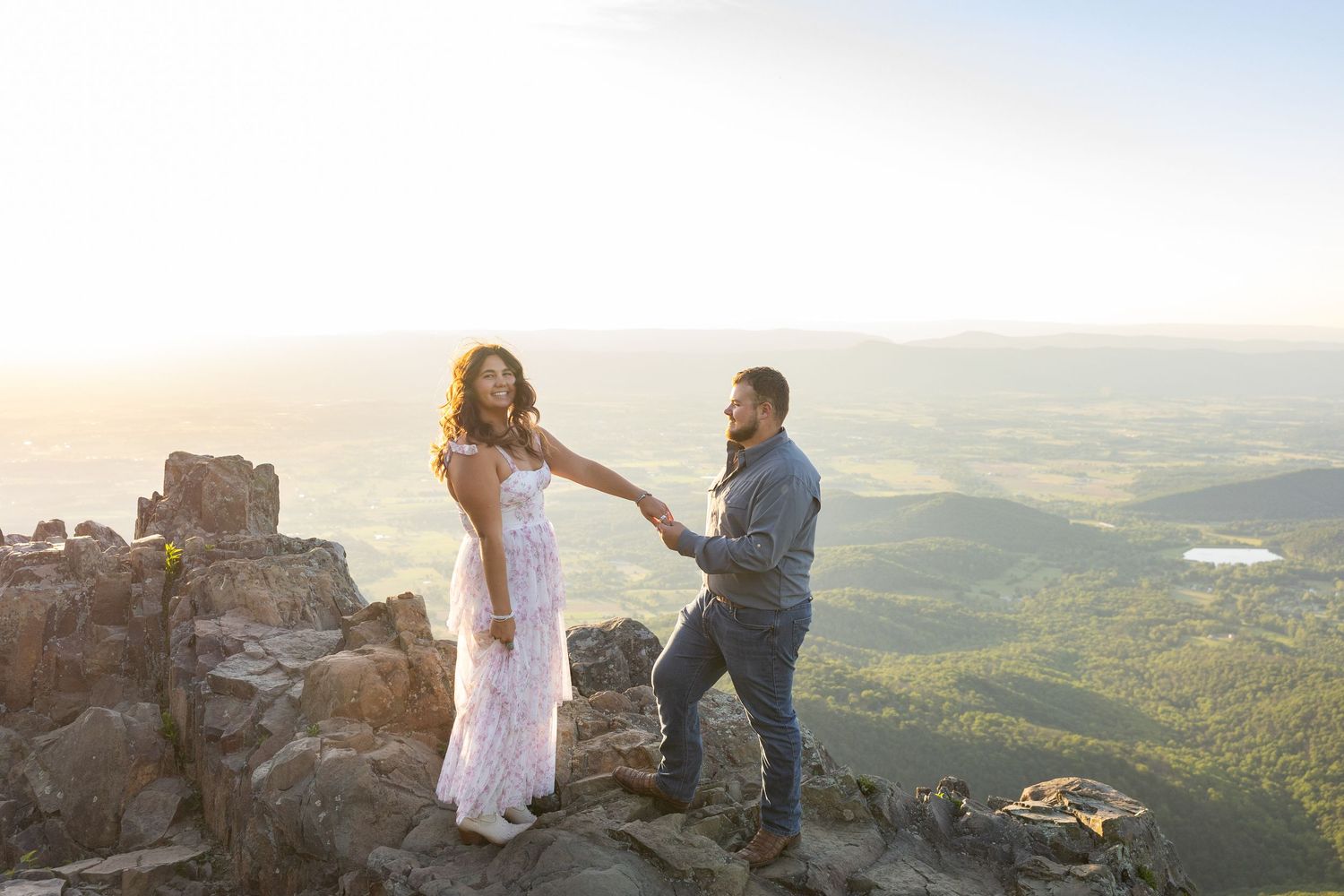 Couple standing on a rocky overlook at Stony Man Mountain Summit at golden hour sunset, after an engagement proposal.