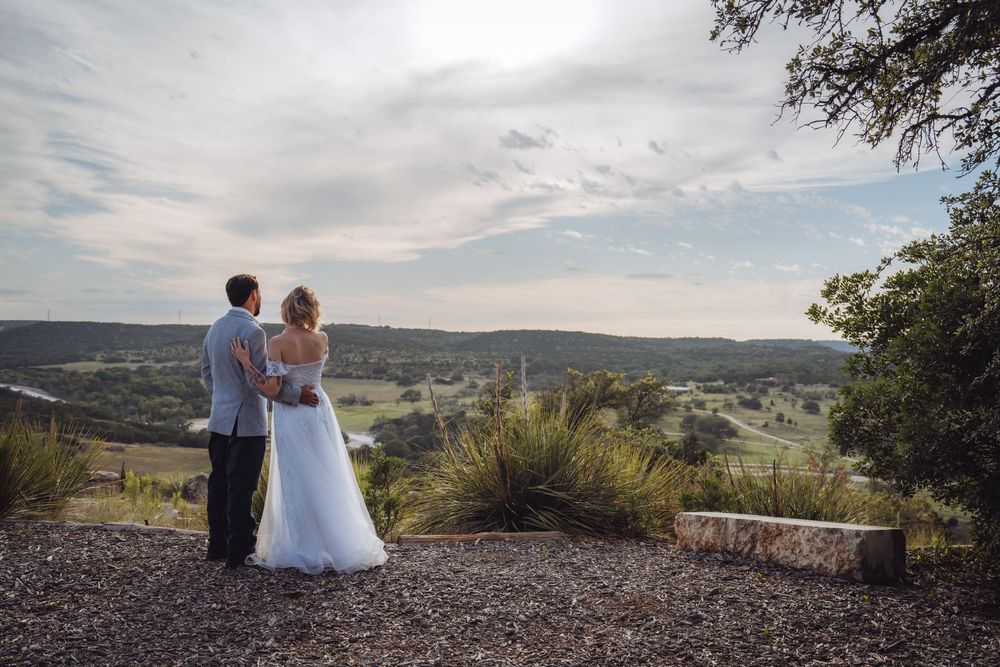 Bride and groom stand together overlooking a scenic Texas Hill Country valley landscape on their wedding day.