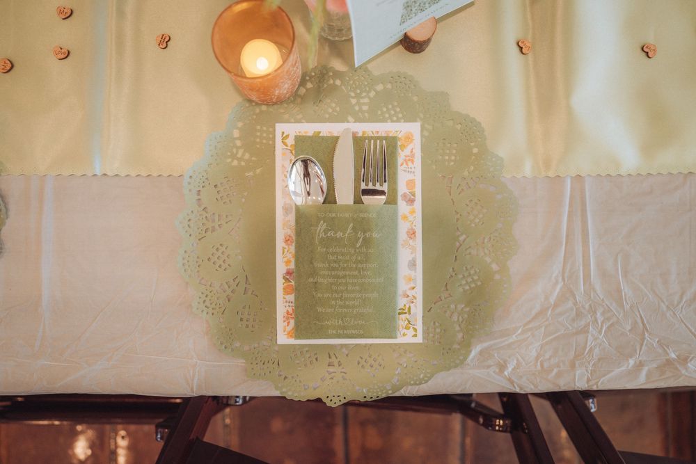 Elegant wedding place setting with green menu card, silverware on lace doily under warm candlelight.