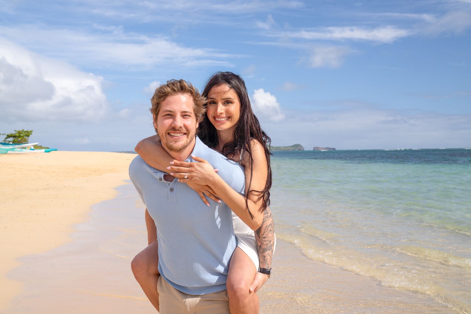 Happy couple enjoying a piggyback ride on a tropical beach with turquoise water and blue sky.