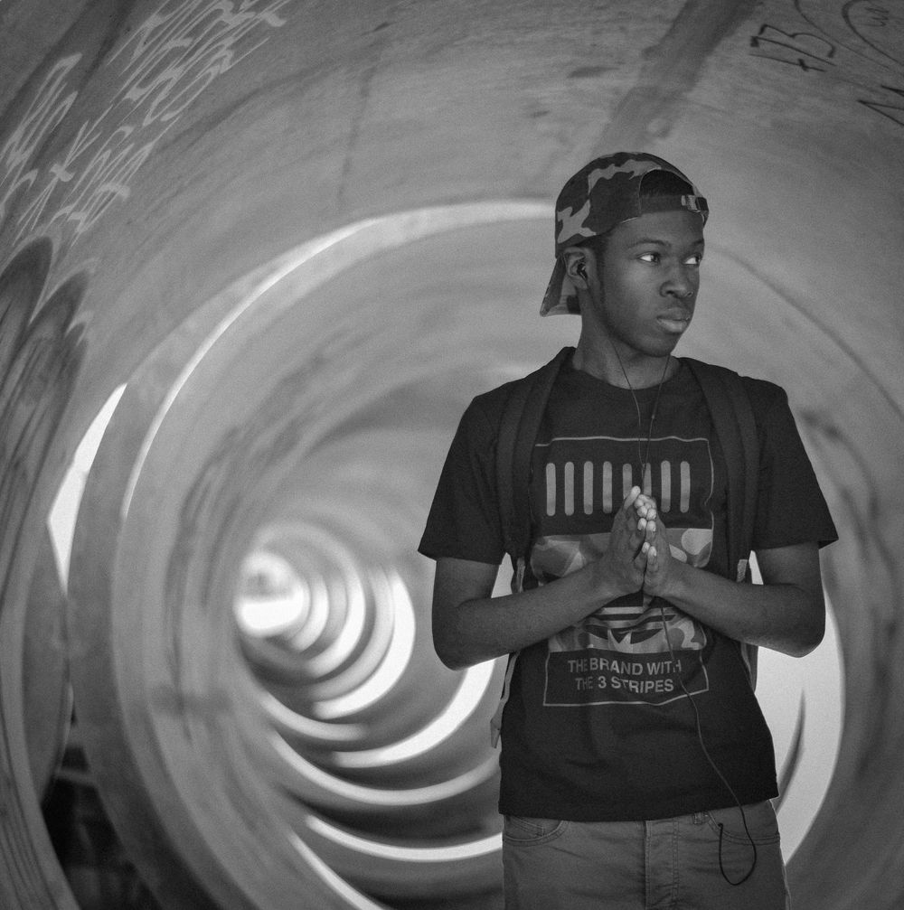 Young man in graphic tee stands inside a large spiral tunnel, black and white photography.