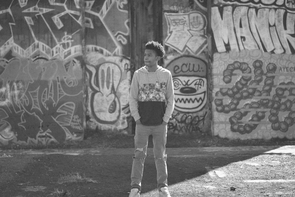 Young person standing in front of a graffiti-covered wall in a black and white urban street photo.