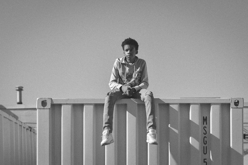 Young man sitting on top of a shipping container in a casual outfit, black and white urban photography.