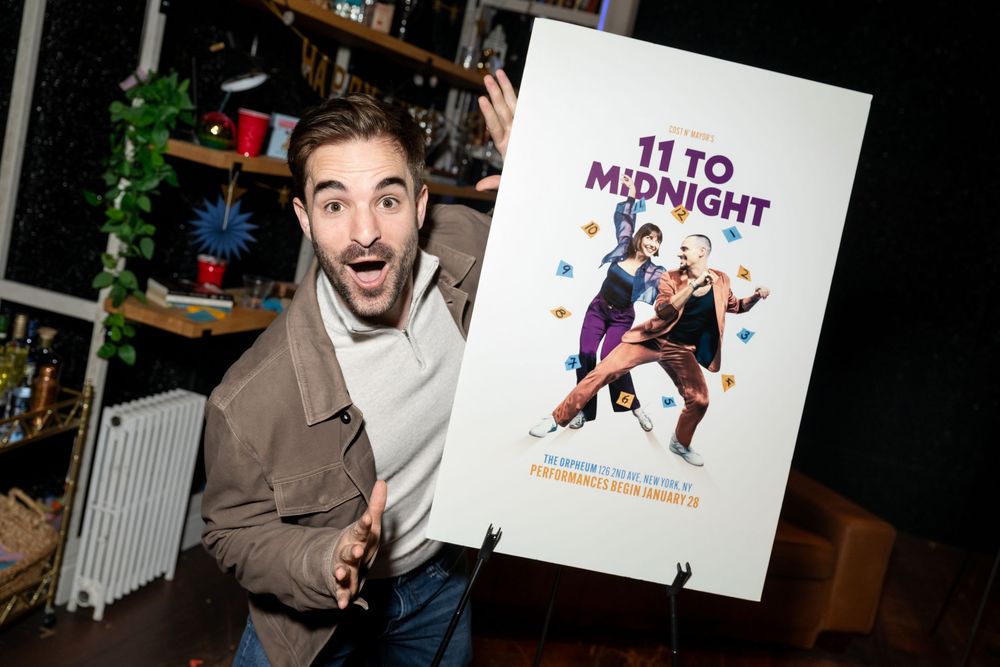 Excited man posing with a promotional poster for the show '11 to Midnight' at an indoor event.