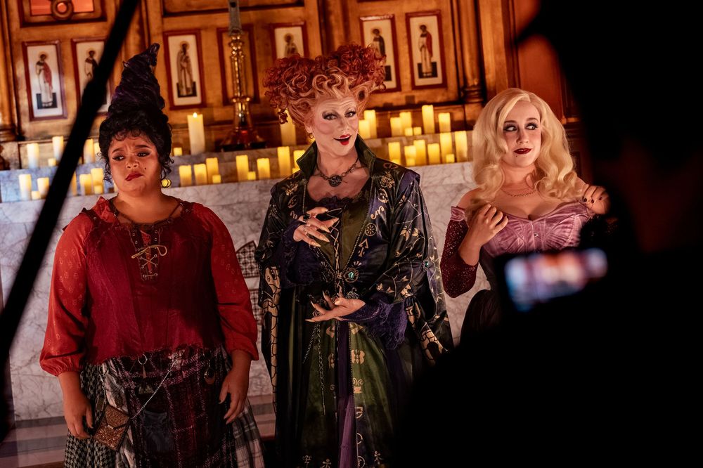 Three women in witch costumes pose dramatically in a candlelit room during a Halloween-themed photoshoot.