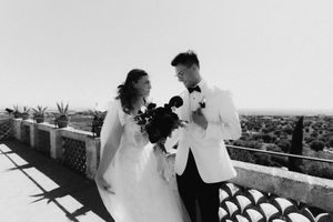 Black and white photo of a bride and groom sharing a joyful moment on a sunlit terrace with a scenic view.