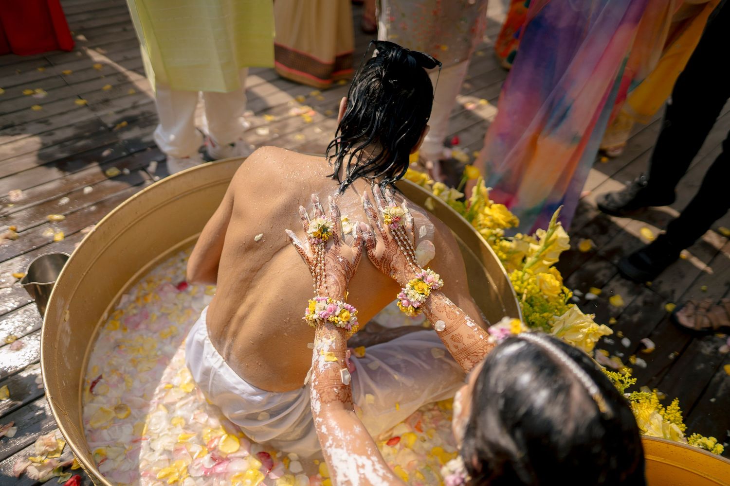 Couple covered in haldi paste during Indian wedding ceremony with guests throwing flowers.