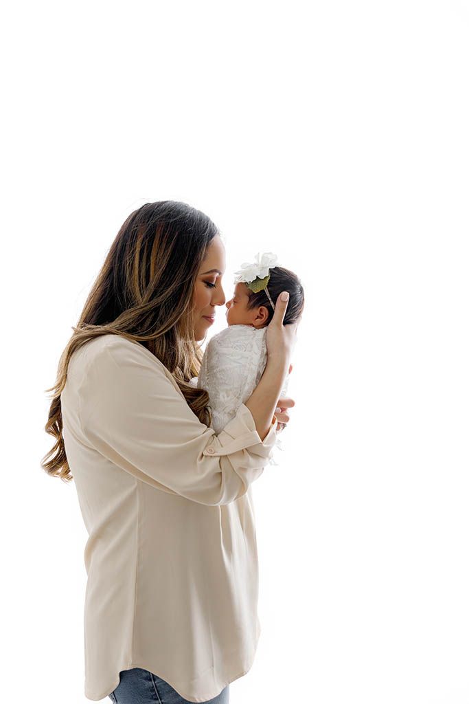 A mother tenderly holds her newborn baby close, touching foreheads in an intimate moment against a white background.