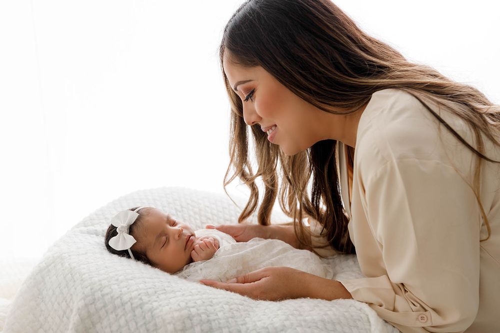 Loving mother gazing at her newborn baby wrapped in white on a soft blanket.