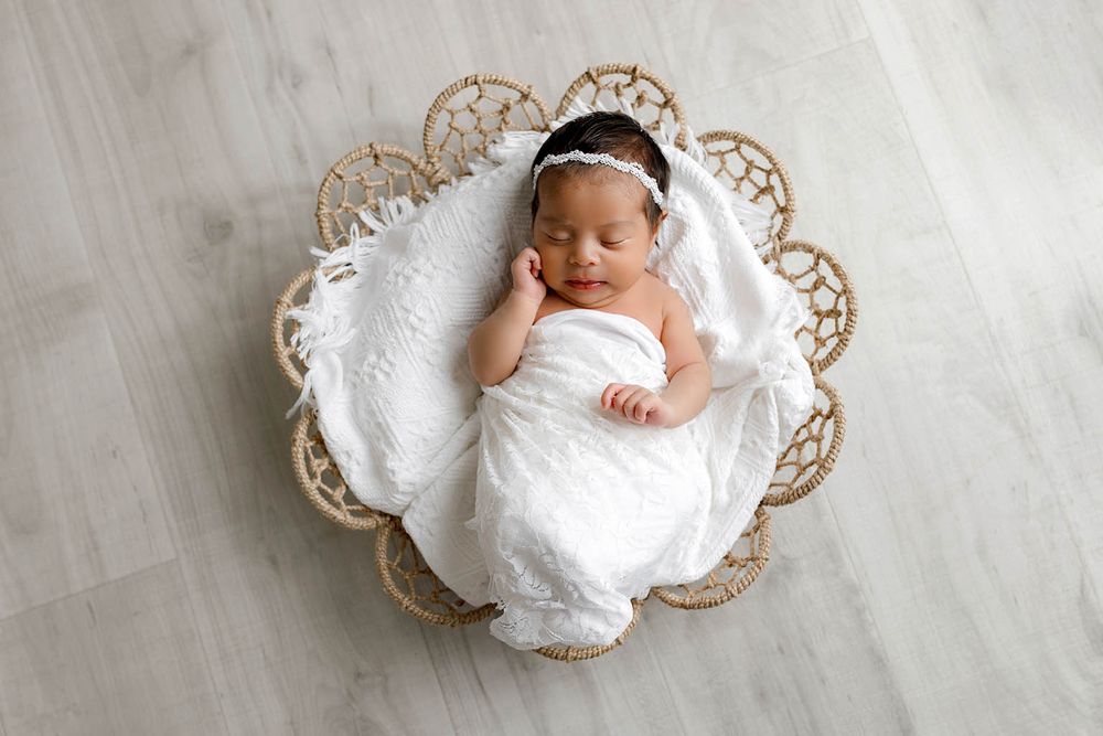 Sleeping newborn baby swaddled in white wrap lying in decorative wicker basket.