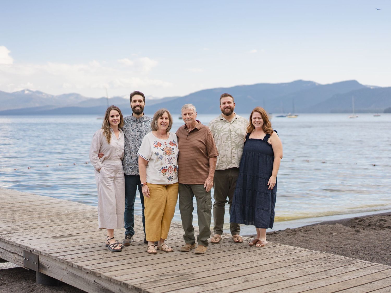 Group of six people posing on a wooden dock with scenic mountain lake views in the background.