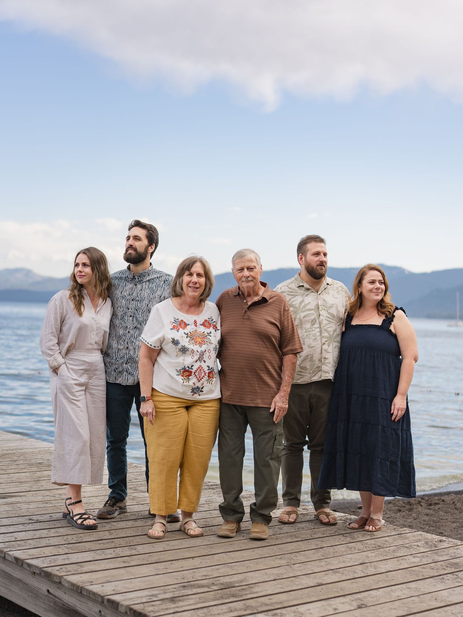 Family of six posing together on a wooden dock by a scenic lake with mountains in the background.