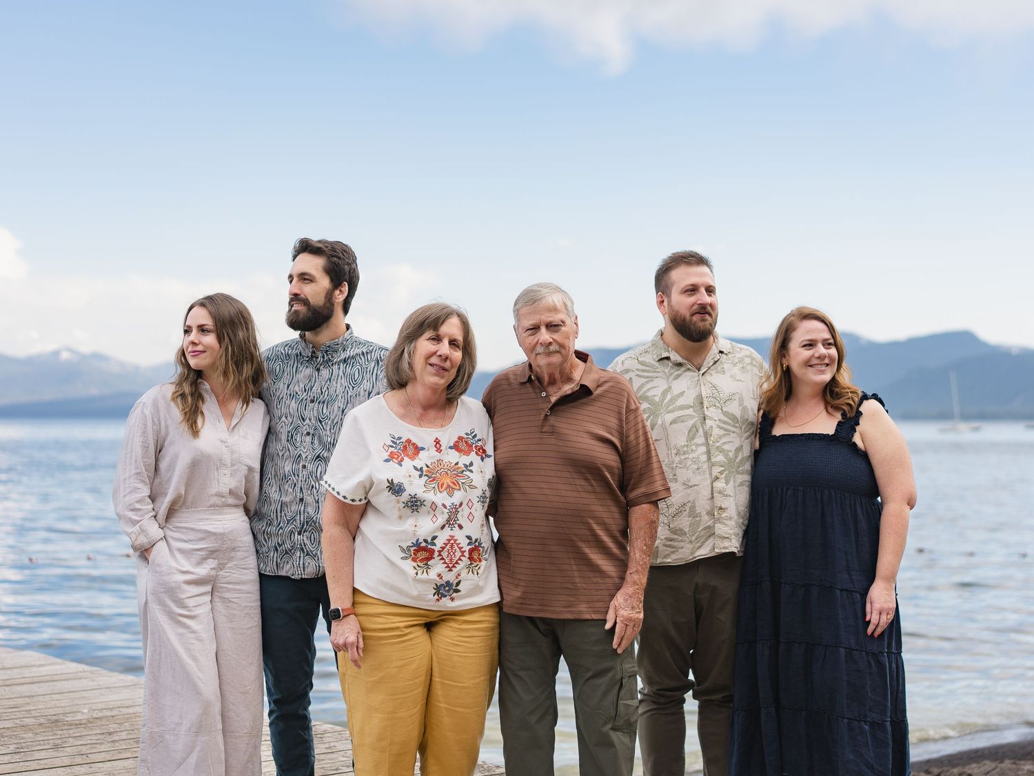 Family of six poses on a lakeside dock with mountain views in background.