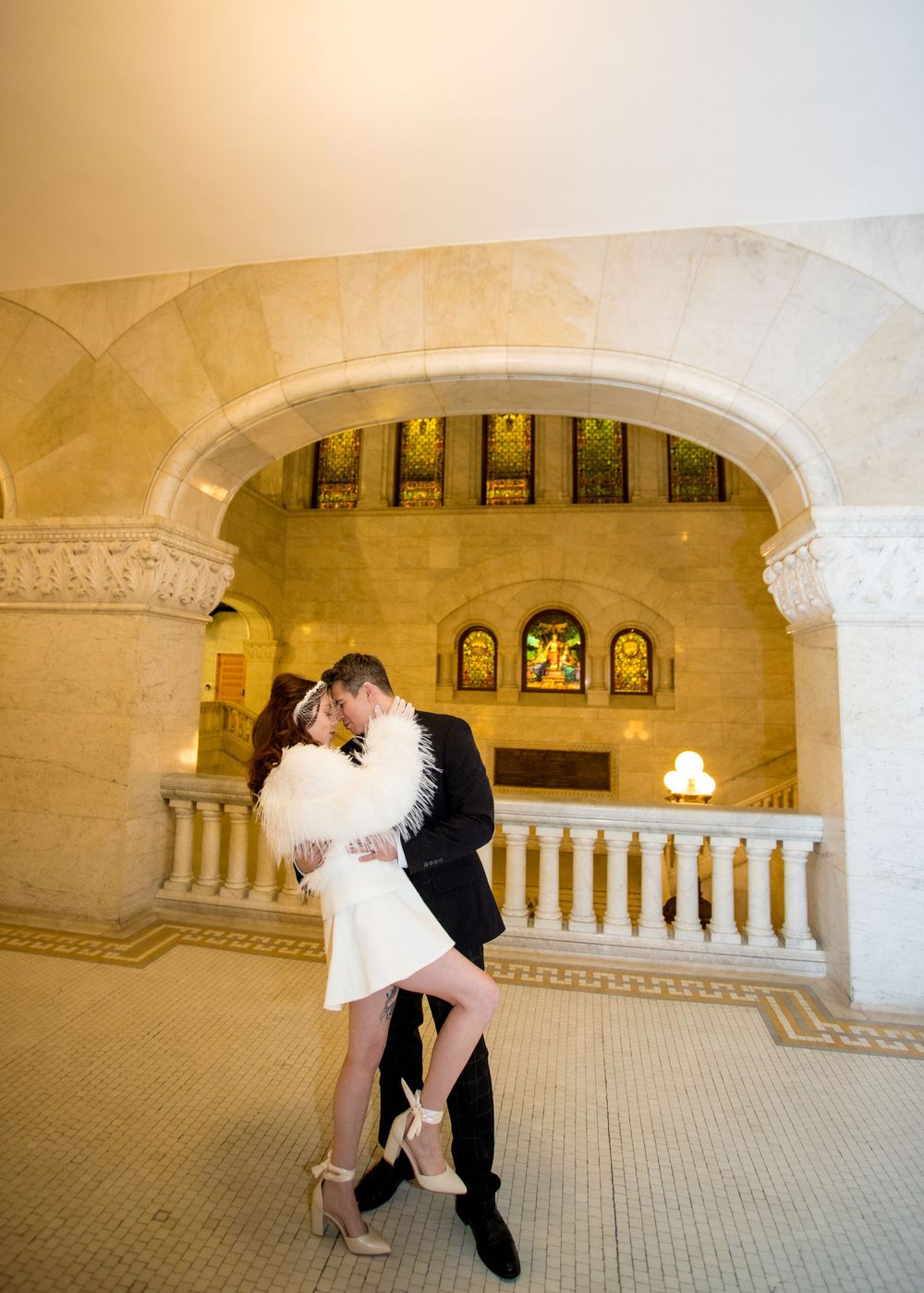 Couple sharing a romantic kiss under a stone arch in an elegant building with stained glass windows.