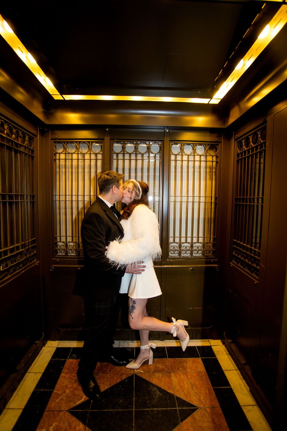 Bride and groom share a romantic kiss inside an elegant vintage elevator with ornate gold details.