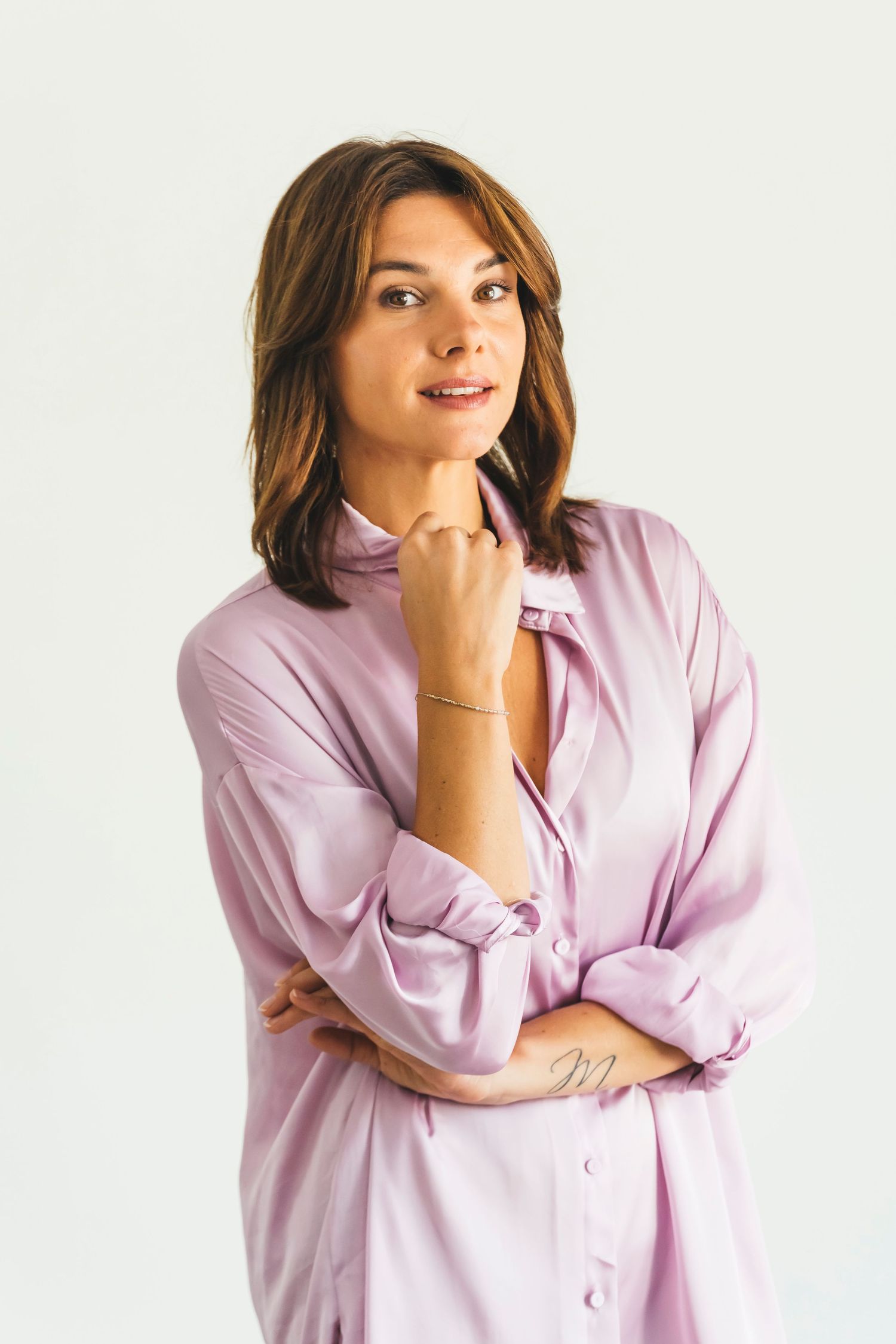 Woman in pink silk shirt posing thoughtfully with hand on chin against white background.