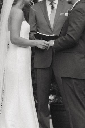Black and white close-up of bride and groom holding hands during outdoor wedding ceremony.