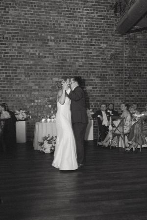 Black and white photo of bride and groom sharing first dance in rustic brick wall reception venue.
