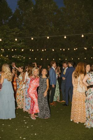 Wedding guests mingling outdoors at night under warm string lights in colorful formal attire.