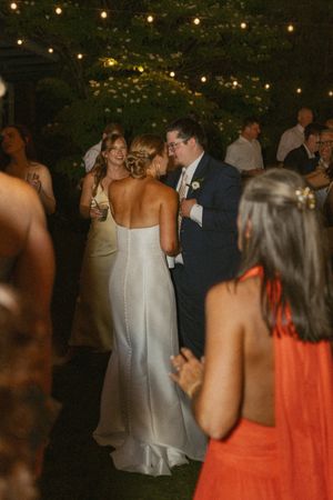 Bride and groom share first dance under string lights at elegant outdoor wedding reception.