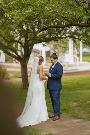 Bride and groom share a romantic first look moment under a lush green tree in a park setting.
