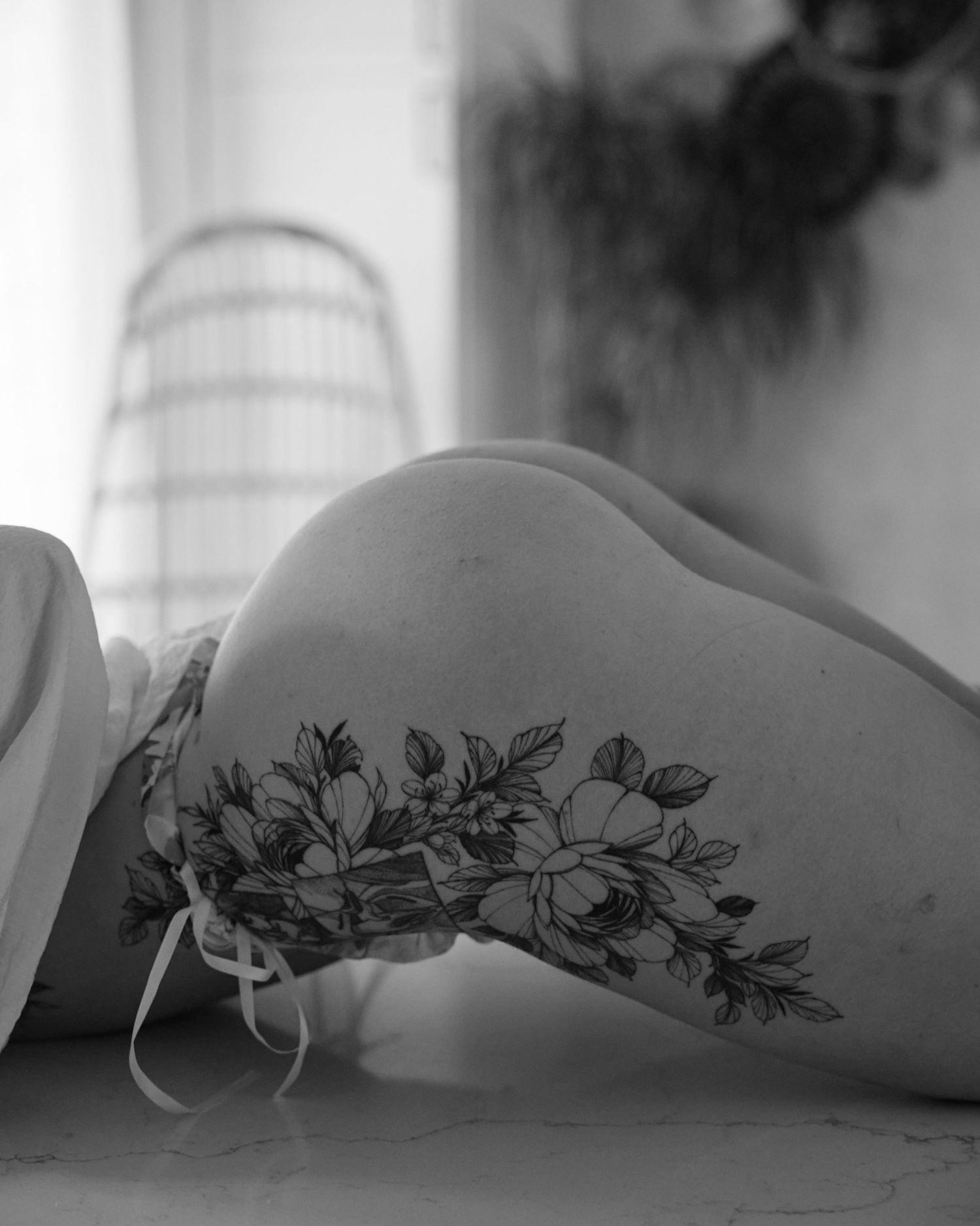 Black and white photo of a floral tattoo on a hip, featuring detailed botanical line art.