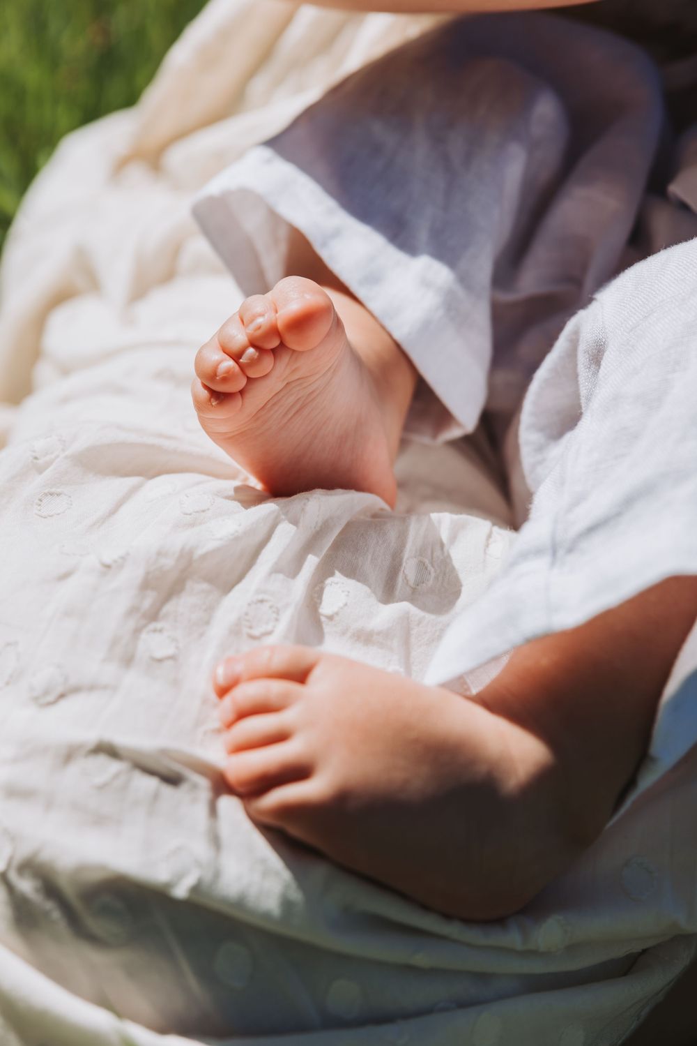 Close-up of tiny baby feet resting on a soft white blanket in warm sunlight outdoors. Lifestyle shoot.