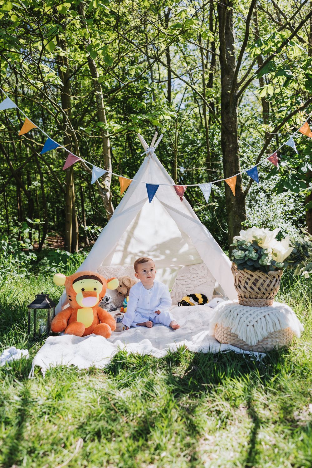 Styled outdoor first birthday photoshoot in a Nieuw-Vennep park featuring boho decor - white tepee tent, baskets, flowers and toys.