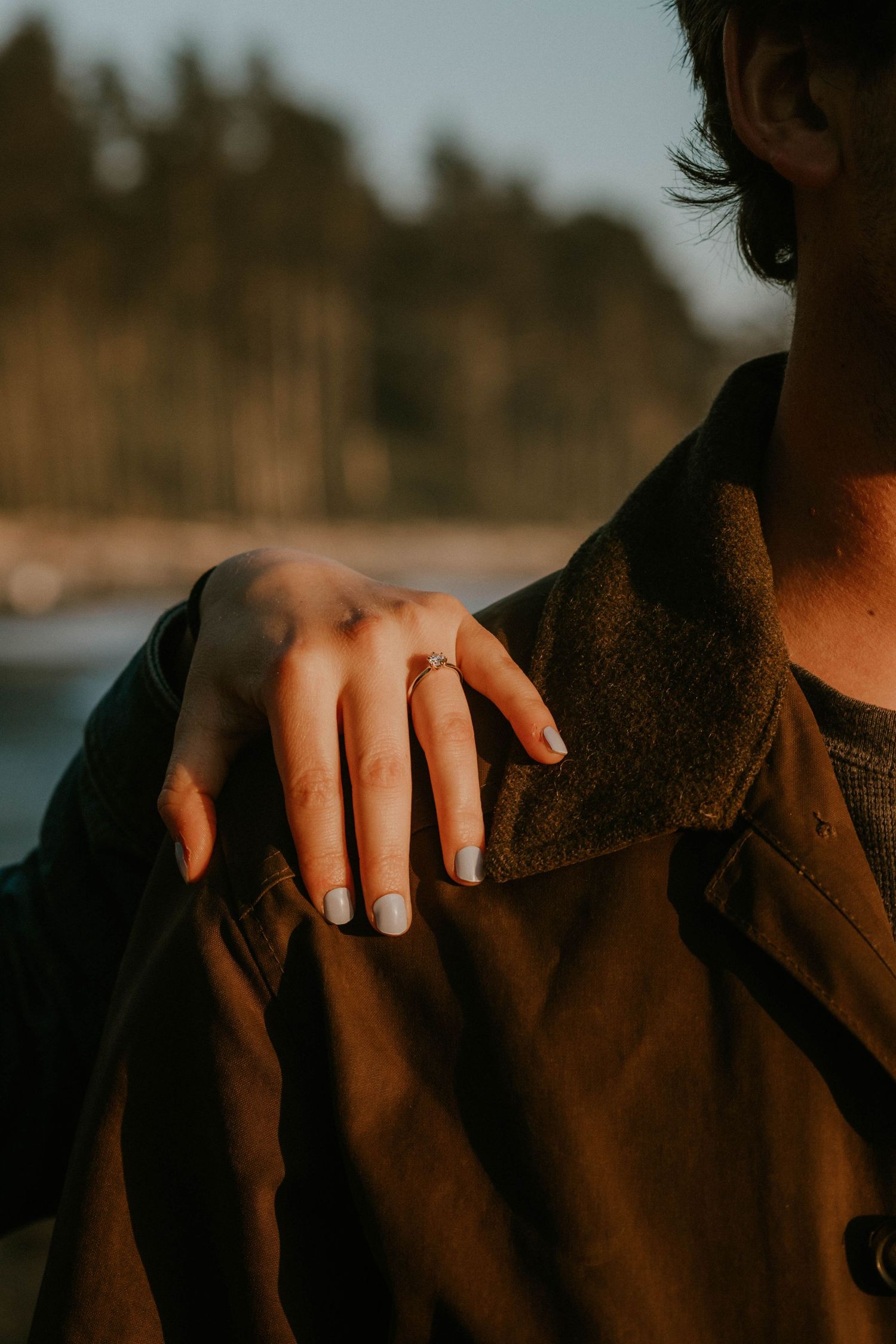 Couple holding hands tenderly, woman with blue nails and gold ring, wearing denim jacket and white pants.