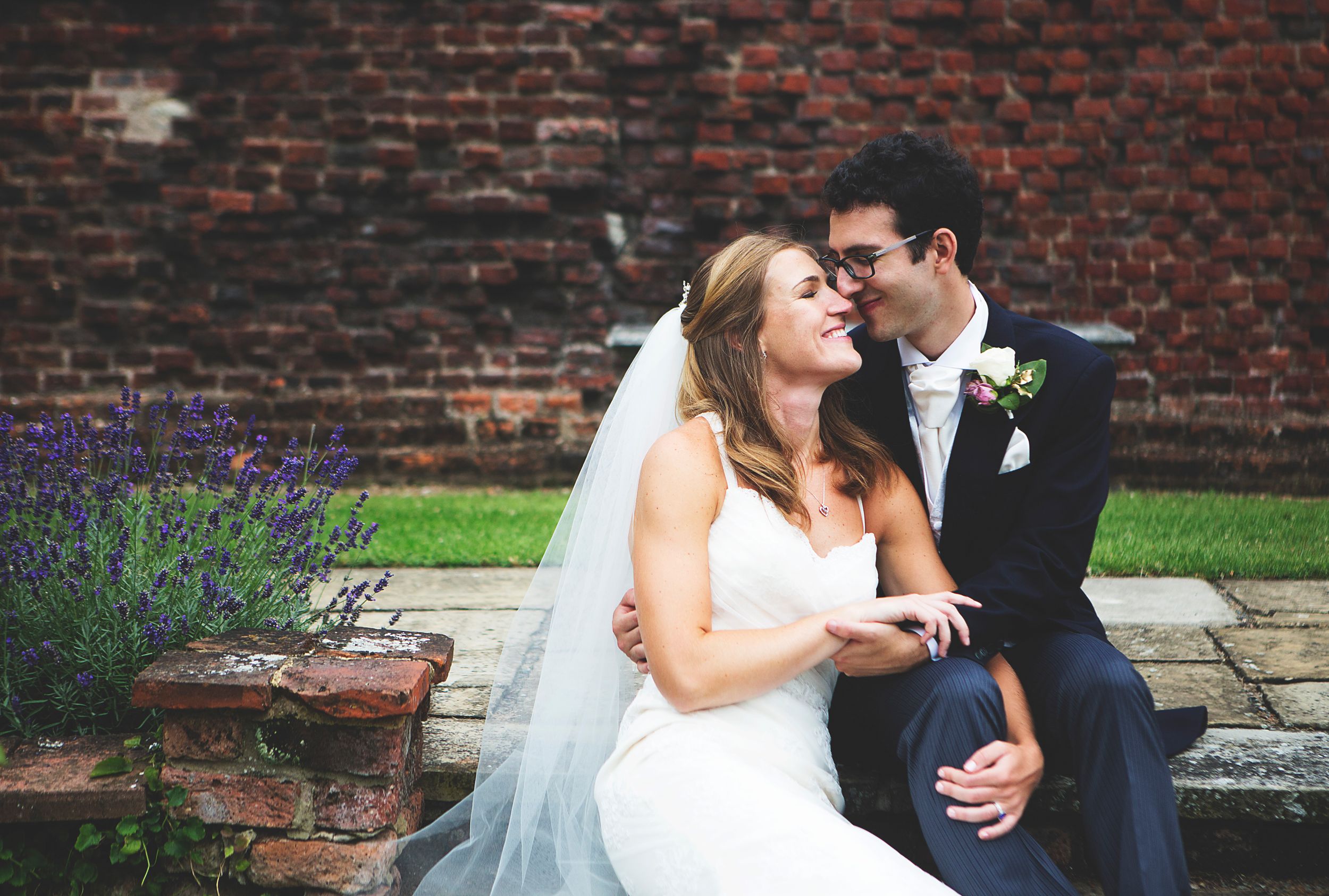 Newlywed couple exits wedding venue as guests throw confetti, bride in white gown, groom in military uniform.