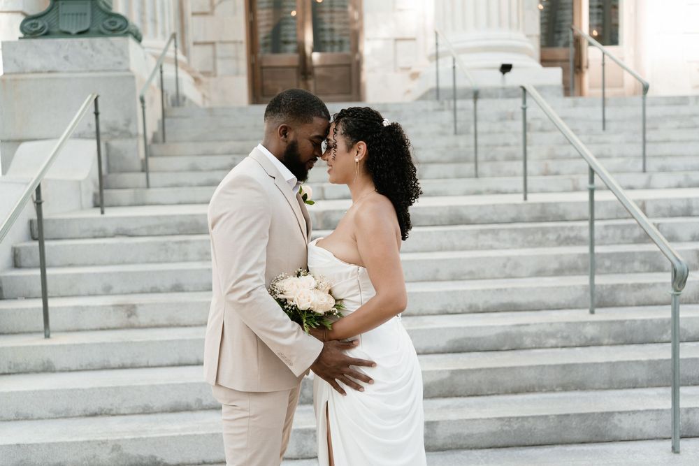 Bride and groom share a romantic moment on stone steps, bride holding white bouquet in elegant white gown.