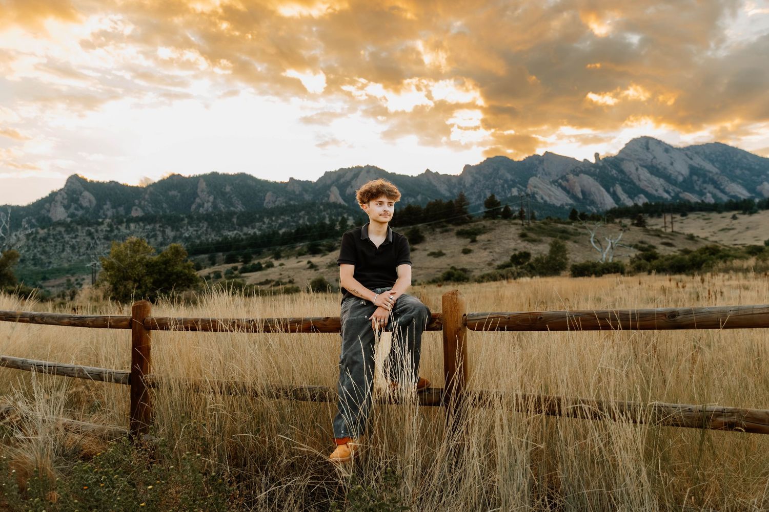 Boy poses sitting down on fence for sunset senior photos and portraits in Boulder, Colorado outside and in nature photos