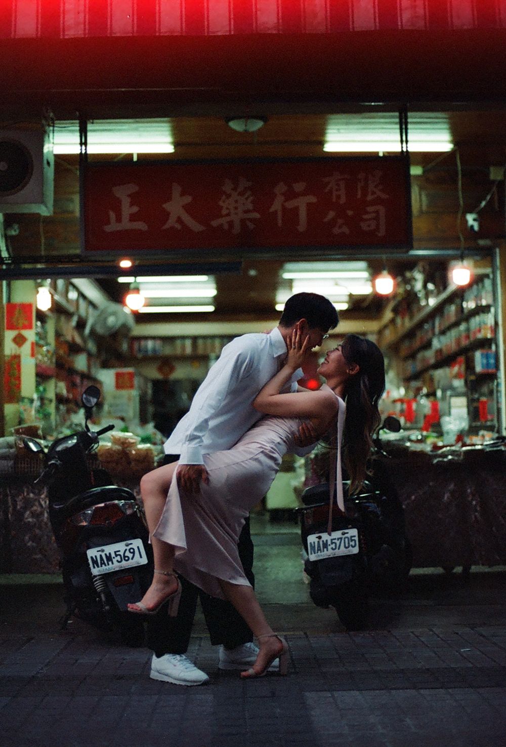 Romantic couple sharing a passionate kiss outside a traditional Chinese pharmacy shop at night in Taiwan.