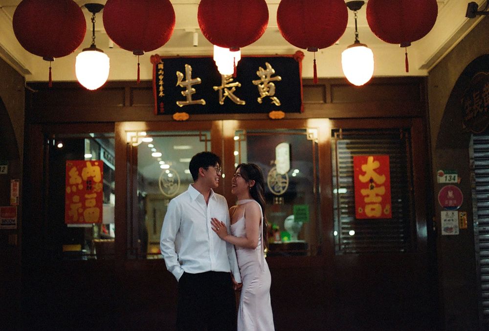 Romantic couple sharing an intimate moment under red lanterns outside a traditional Chinese storefront at night.