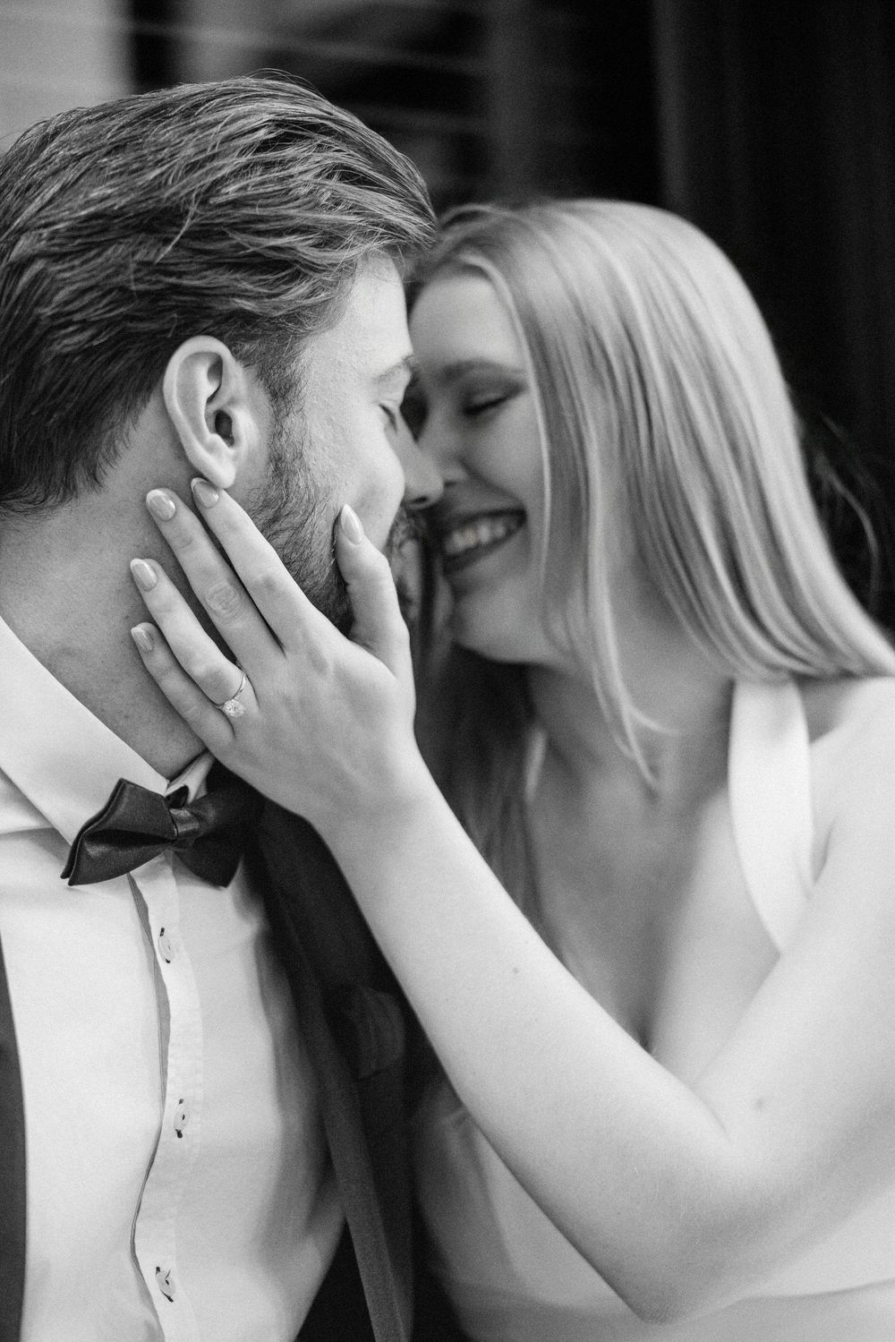 Black and white photo of a smiling bride touching grooms face, sharing a romantic moment in wedding attire.