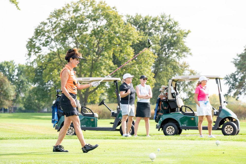 Golfers and golf carts on sunny course fairway during outdoor golf outing event.