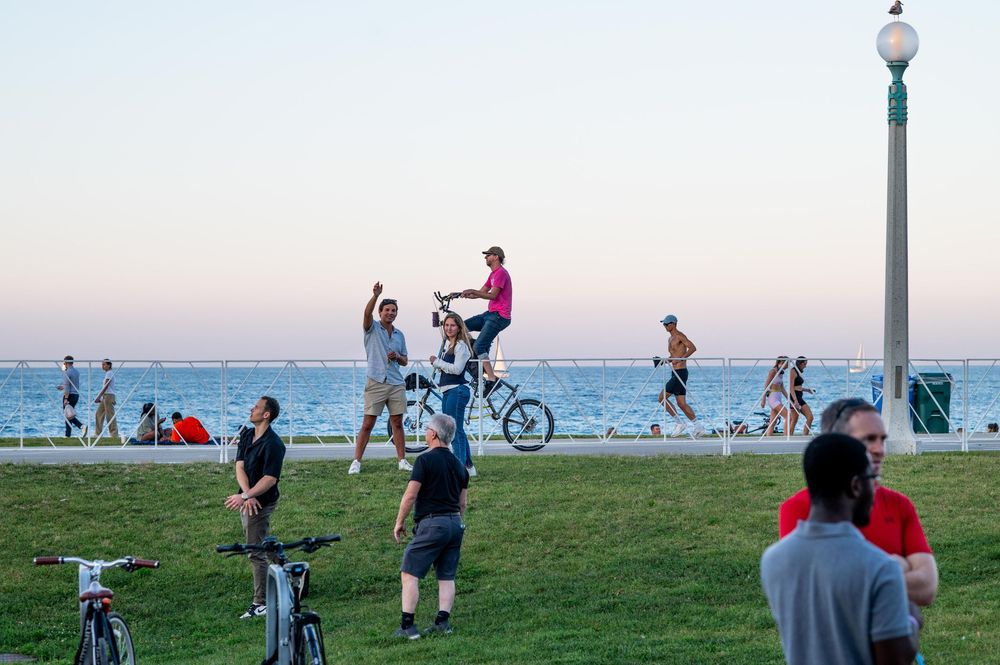 People enjoying outdoor activities near the waterfront at dusk, with cyclists and pedestrians on a seaside promenade.