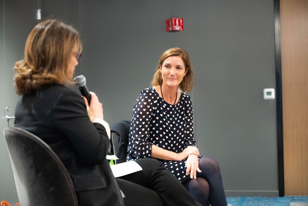 Two women engage in a panel discussion, one holding a microphone in a modern conference room setting.