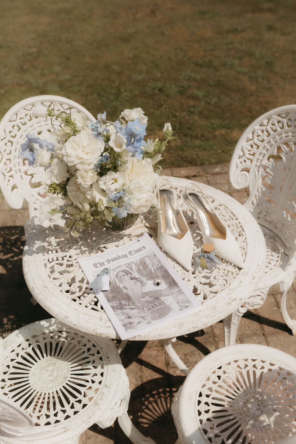 White iron garden table with bridal bouquet, heels, and Sunday Times newspaper in sunlight.