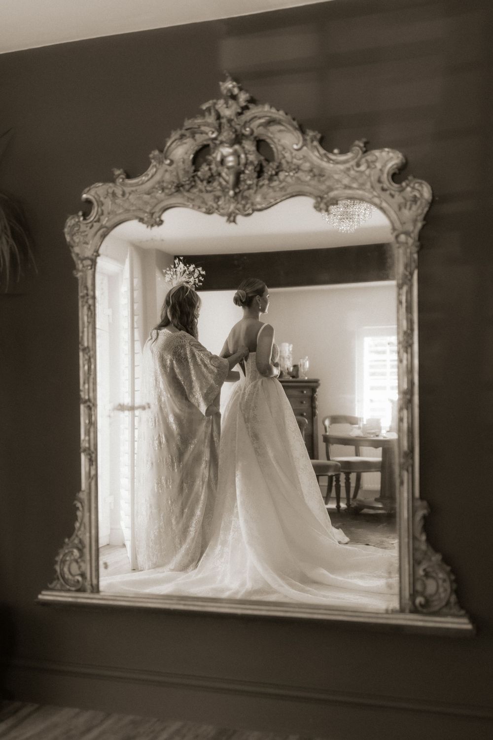 Bride getting ready reflected in ornate gold baroque mirror, sepia toned wedding photography.