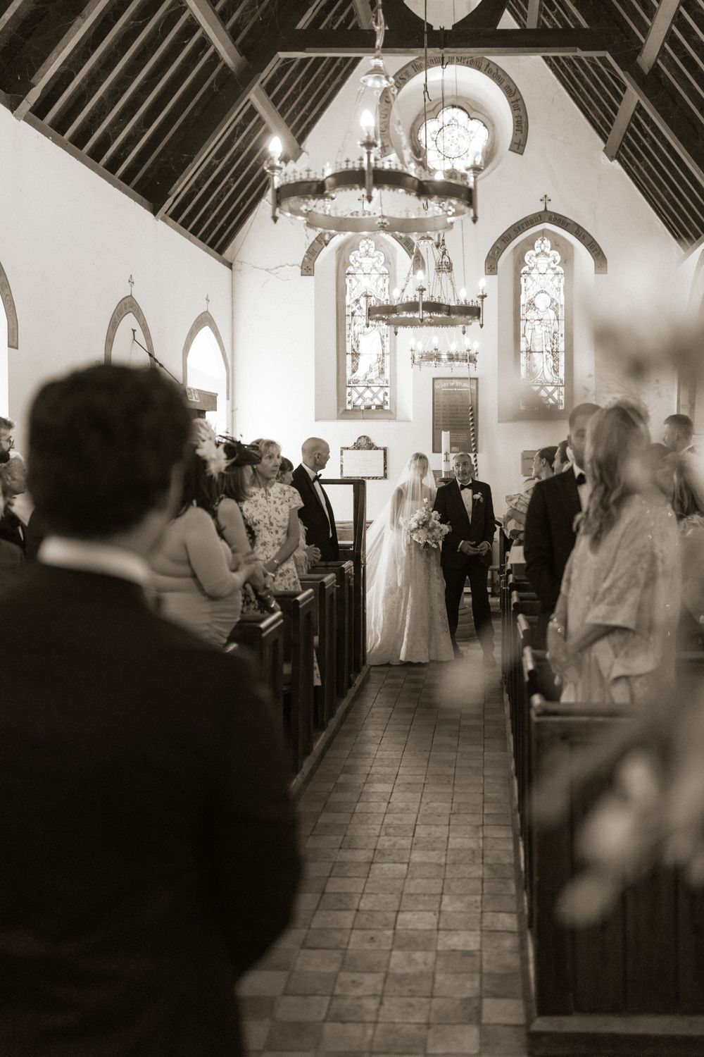 Bride walking down the aisle of a historic church with stained glass windows during wedding ceremony.