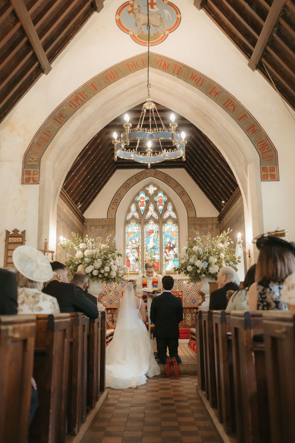 Bride and groom at the altar of a charming church with ornate stained glass window and floral arrangements.