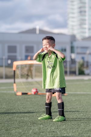 Young boy in green Tim Hortons soccer uniform smiling on a soccer field with goal in background.
